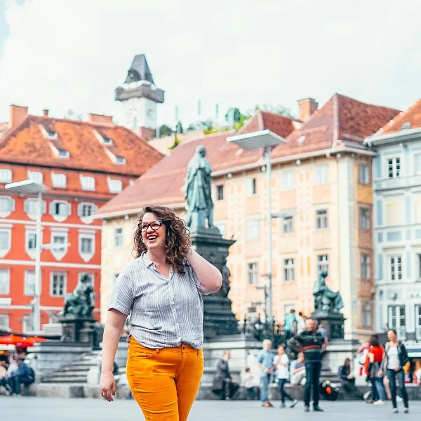 Curvy girl in bright yellow pants with curly hair in a colorful plaza in Graz, Austria